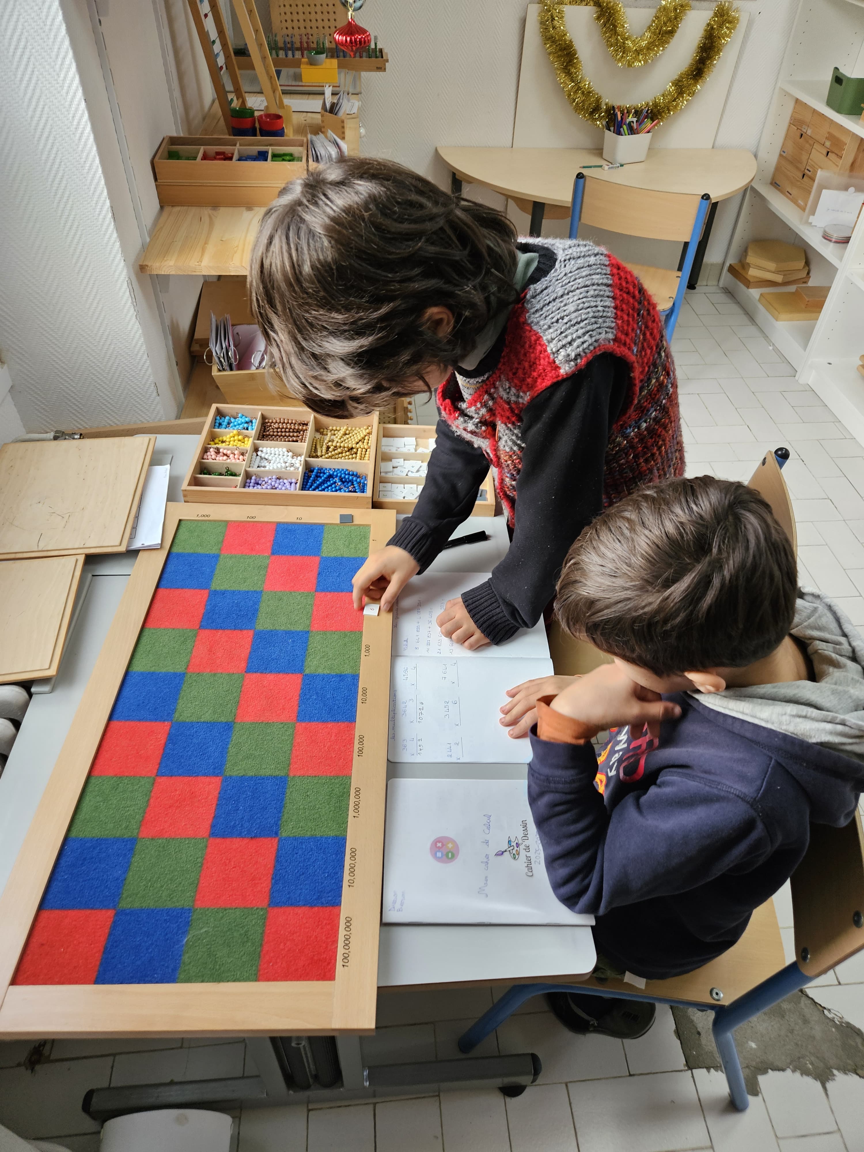 Deux enfants travaillent avec le damier des multiplications Montessori